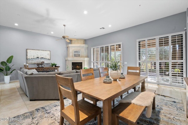 dining space featuring ceiling fan, a fireplace, and light tile patterned floors