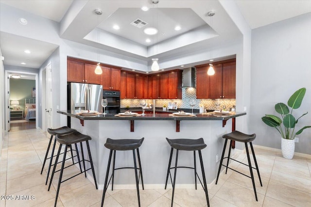 kitchen with wall chimney exhaust hood, hanging light fixtures, stainless steel fridge with ice dispenser, a breakfast bar, and double oven