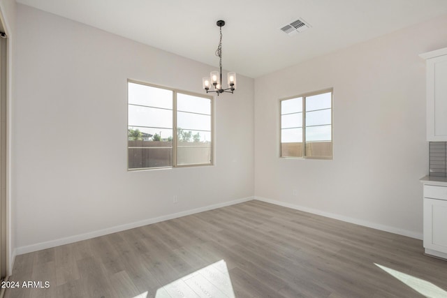 unfurnished dining area with a healthy amount of sunlight, a notable chandelier, and light wood-type flooring