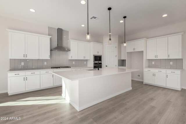 kitchen featuring sink, a center island with sink, wall chimney exhaust hood, and light hardwood / wood-style floors