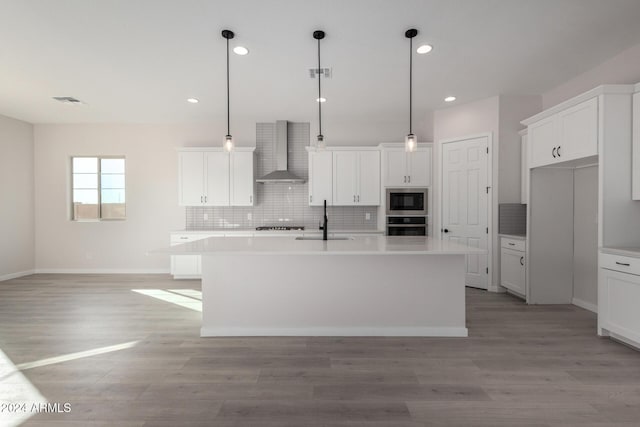 kitchen with appliances with stainless steel finishes, sink, a kitchen island with sink, and wall chimney range hood