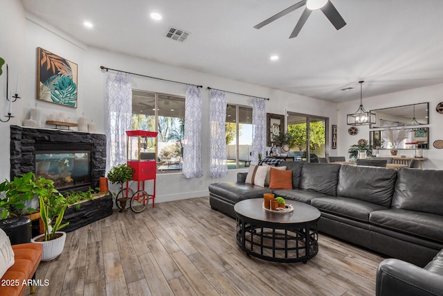 living room featuring a stone fireplace, ceiling fan with notable chandelier, and light wood-type flooring