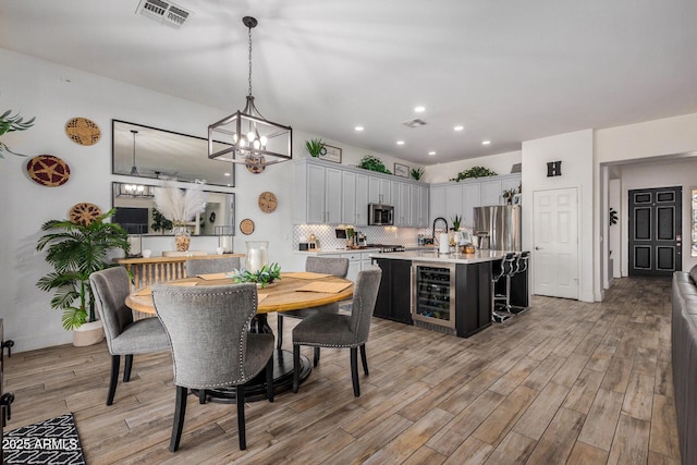 dining area with sink, light hardwood / wood-style flooring, beverage cooler, and a chandelier