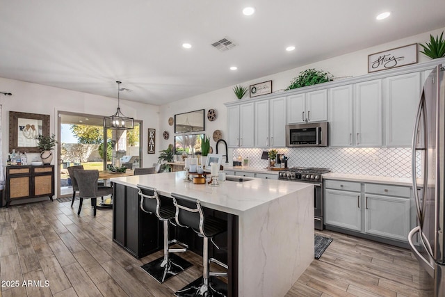 kitchen featuring appliances with stainless steel finishes, decorative light fixtures, sink, light stone countertops, and a center island with sink