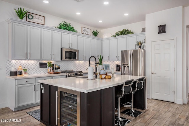 kitchen featuring appliances with stainless steel finishes, a center island with sink, wine cooler, a kitchen bar, and light wood-type flooring