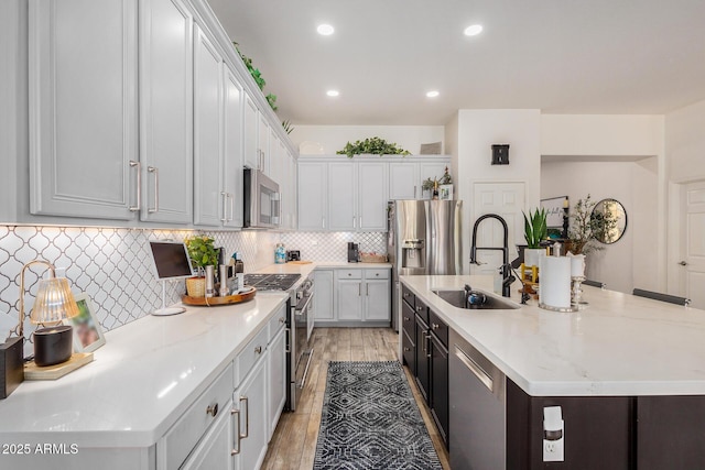 kitchen with sink, a center island with sink, light hardwood / wood-style floors, and appliances with stainless steel finishes