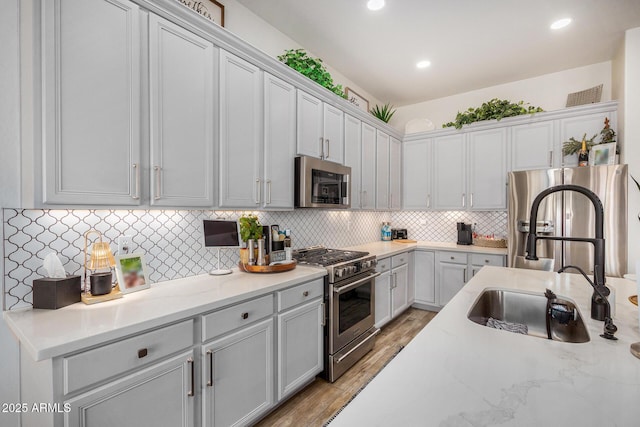 kitchen with sink, appliances with stainless steel finishes, backsplash, light stone countertops, and light wood-type flooring