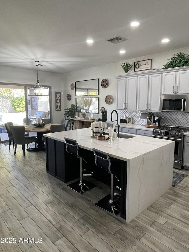 kitchen with white cabinetry, decorative light fixtures, a center island with sink, and appliances with stainless steel finishes