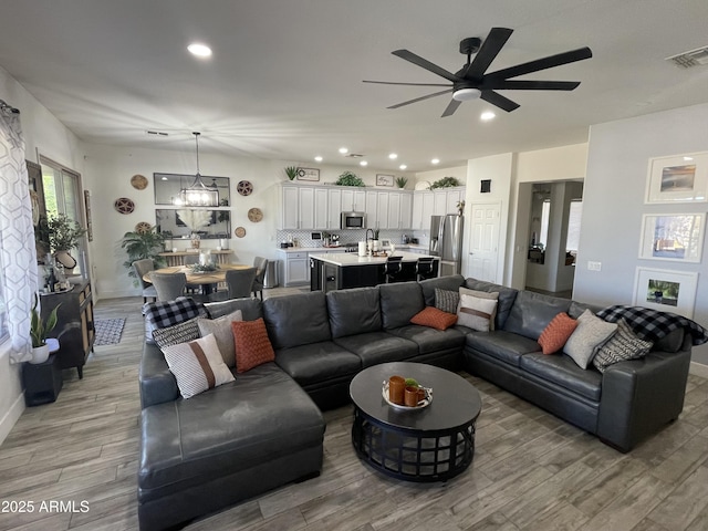 living room featuring ceiling fan with notable chandelier and light hardwood / wood-style floors