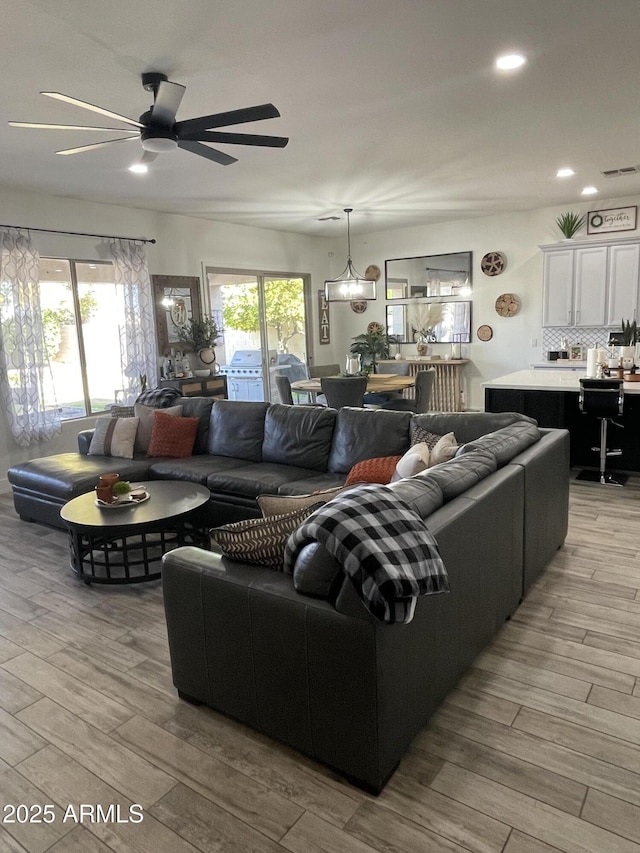 living room featuring ceiling fan with notable chandelier and light wood-type flooring