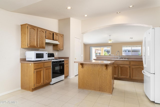 kitchen featuring sink, white appliances, a kitchen breakfast bar, a kitchen island, and ceiling fan