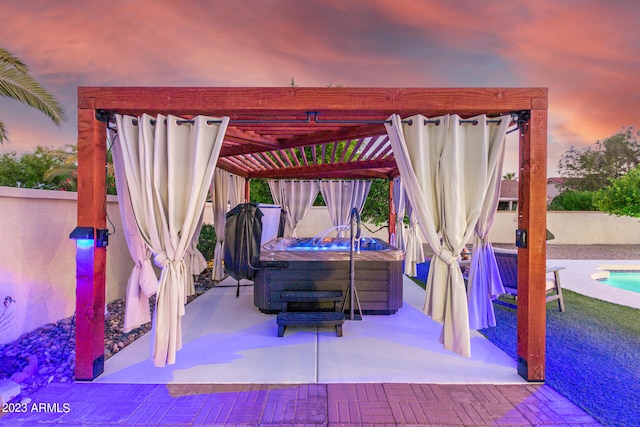 patio terrace at dusk with a hot tub and a pergola