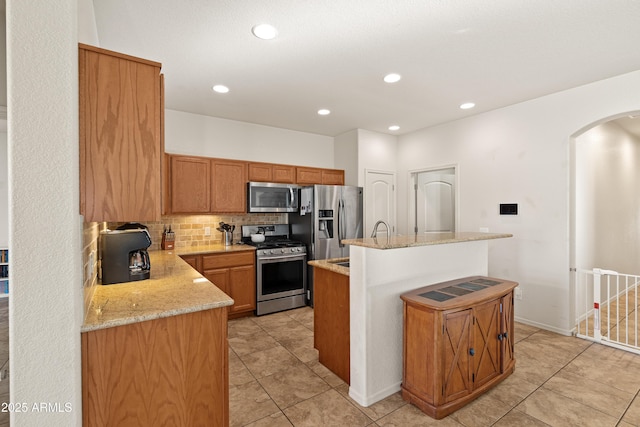 kitchen with decorative backsplash, appliances with stainless steel finishes, light stone counters, light tile patterned floors, and a center island with sink