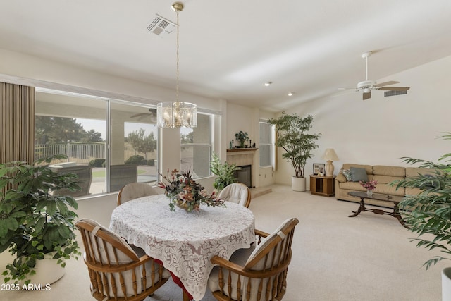 dining space with ceiling fan with notable chandelier, light carpet, lofted ceiling, and a fireplace