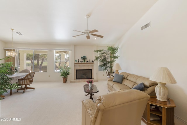 living room featuring lofted ceiling, ceiling fan with notable chandelier, carpet floors, and a tile fireplace