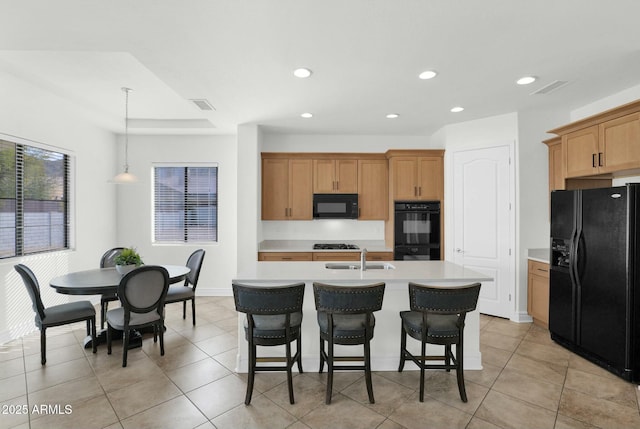 kitchen with decorative light fixtures, sink, a kitchen breakfast bar, a kitchen island with sink, and black appliances