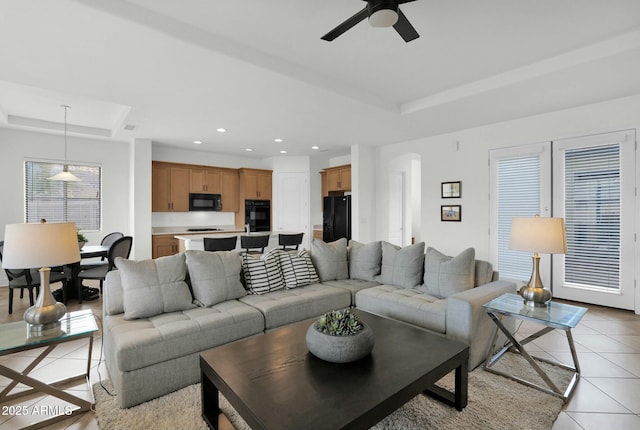 living room featuring a raised ceiling, ceiling fan, and light tile patterned flooring