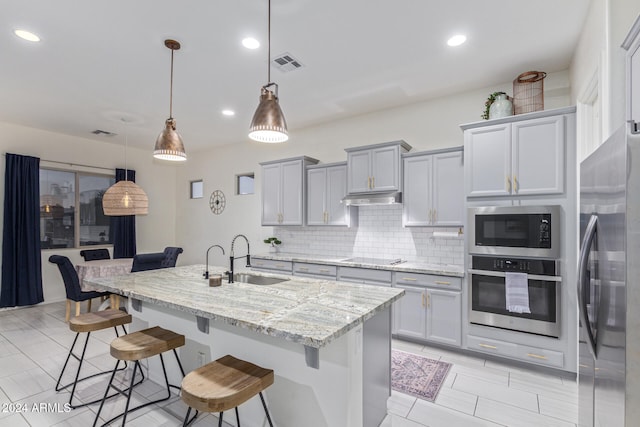 kitchen featuring sink, stainless steel appliances, decorative light fixtures, a kitchen bar, and a center island with sink