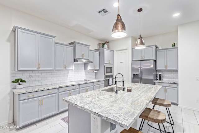 kitchen featuring backsplash, an island with sink, appliances with stainless steel finishes, decorative light fixtures, and a kitchen bar