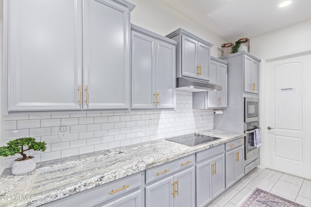 kitchen featuring appliances with stainless steel finishes, tasteful backsplash, light stone counters, gray cabinetry, and light tile patterned flooring