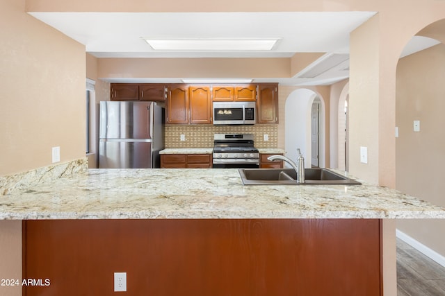 kitchen with kitchen peninsula, appliances with stainless steel finishes, sink, and backsplash