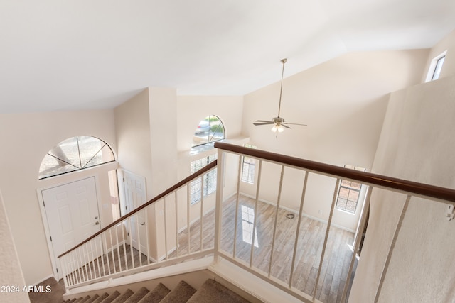 stairway with ceiling fan, wood-type flooring, and high vaulted ceiling