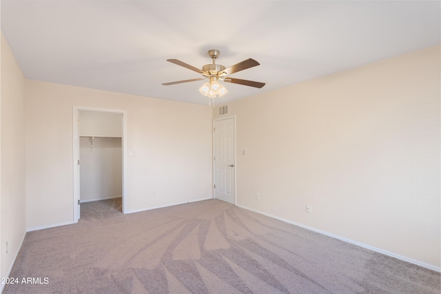 unfurnished bedroom featuring light carpet, ceiling fan, a walk in closet, and a closet