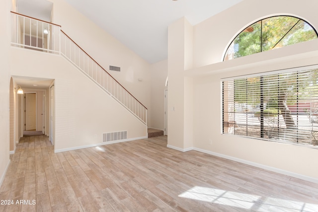 unfurnished living room featuring light wood-type flooring and a towering ceiling