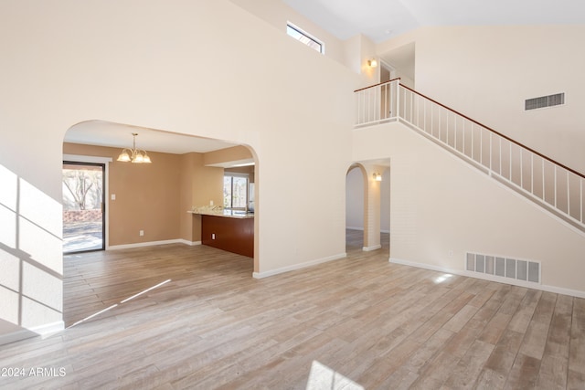 unfurnished living room featuring light hardwood / wood-style floors, an inviting chandelier, and high vaulted ceiling