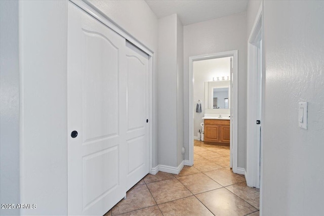 corridor with light tile patterned flooring, baseboards, and a sink