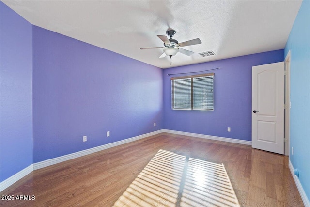 spare room featuring wood finished floors, visible vents, baseboards, ceiling fan, and a textured ceiling