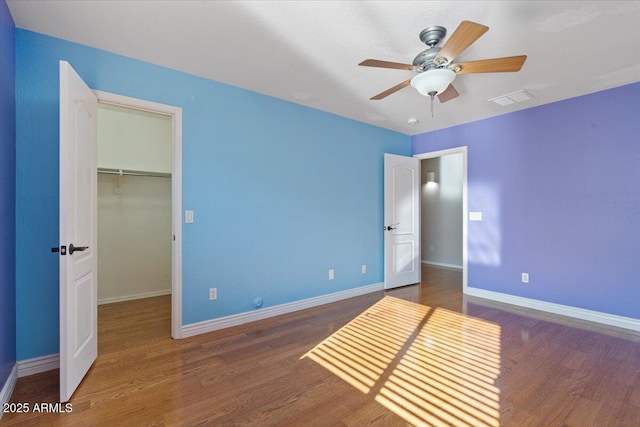 unfurnished bedroom featuring visible vents, a walk in closet, baseboards, and wood finished floors