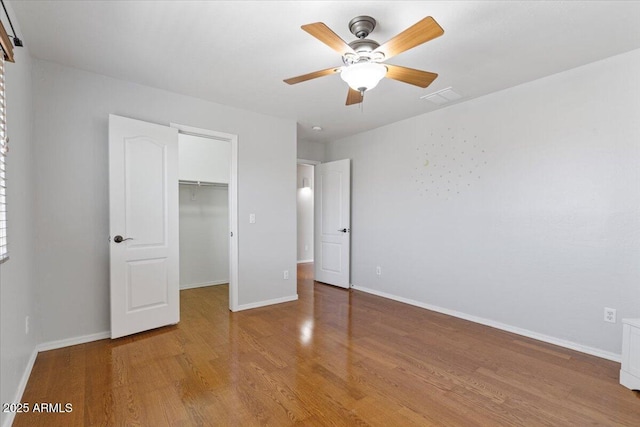 unfurnished bedroom featuring a closet, baseboards, wood finished floors, and a spacious closet