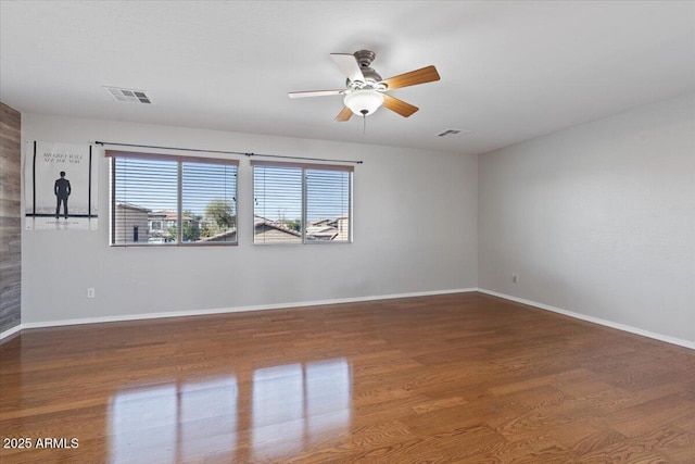 empty room with wood finished floors, visible vents, and baseboards