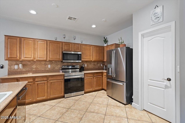 kitchen featuring visible vents, light countertops, light tile patterned floors, appliances with stainless steel finishes, and brown cabinetry