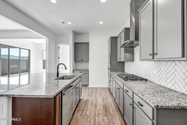 kitchen featuring sink, wall chimney range hood, light stone countertops, and stainless steel appliances