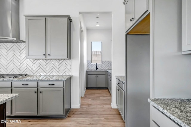 kitchen with wall chimney range hood, gray cabinets, light stone countertops, and stainless steel gas stovetop