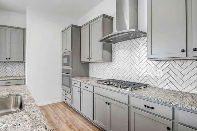 kitchen with stainless steel appliances, gray cabinets, light stone countertops, and wall chimney range hood