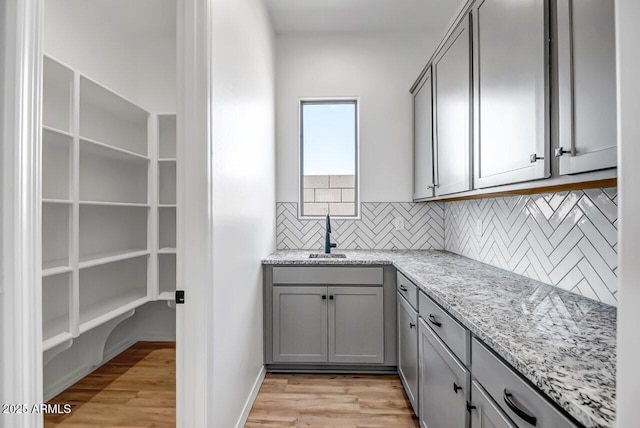 kitchen featuring sink, gray cabinetry, light stone countertops, light hardwood / wood-style floors, and backsplash