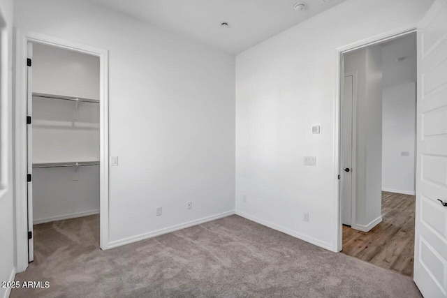 unfurnished bedroom with a walk in closet, a closet, and light carpet