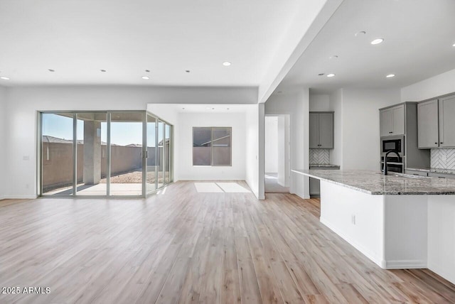 kitchen featuring sink, light stone counters, light wood-type flooring, stainless steel microwave, and gray cabinets