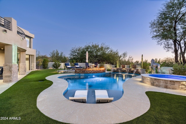 pool at dusk featuring an in ground hot tub, pool water feature, and a lawn