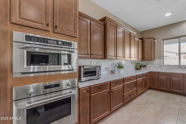 kitchen featuring double oven, light tile patterned floors, light stone countertops, and tasteful backsplash