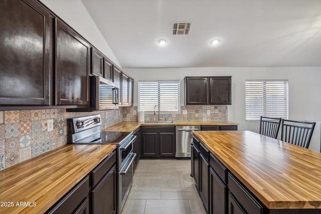 kitchen featuring appliances with stainless steel finishes, lofted ceiling, wooden counters, tasteful backsplash, and sink