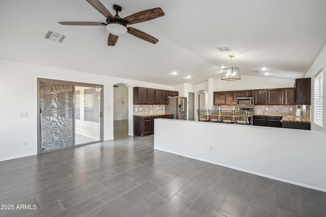 kitchen with ceiling fan with notable chandelier, appliances with stainless steel finishes, decorative light fixtures, decorative backsplash, and vaulted ceiling