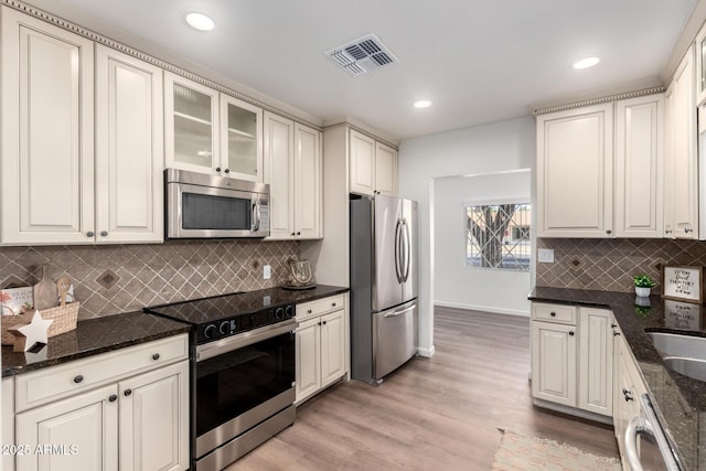 48 S Catalina St, Gilbert, AZ 85233 - kitchen featuring appliances with stainless steel finishes, light wood finished floors, decorative backsplash, dark stone counters, and glass insert cabinets