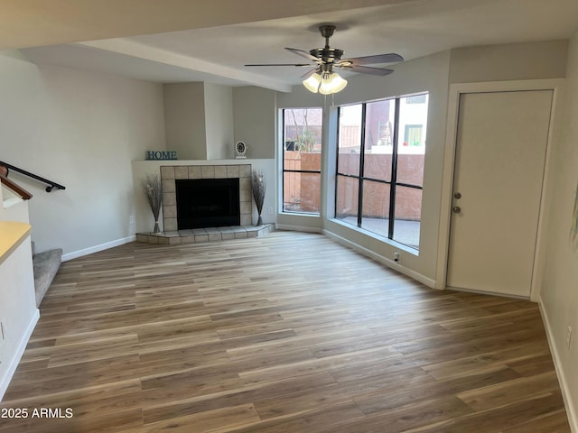 unfurnished living room with a tiled fireplace, hardwood / wood-style floors, and ceiling fan