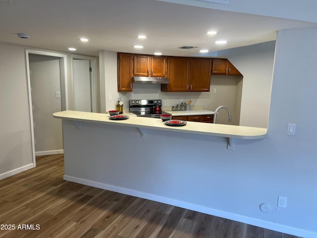 kitchen with dark hardwood / wood-style floors, a breakfast bar area, stainless steel range with electric cooktop, and kitchen peninsula