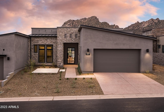 view of front of house featuring driveway, a standing seam roof, stone siding, metal roof, and a garage