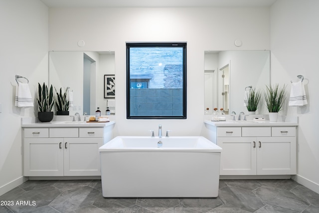 bathroom featuring a sink, two vanities, baseboards, and a freestanding bath